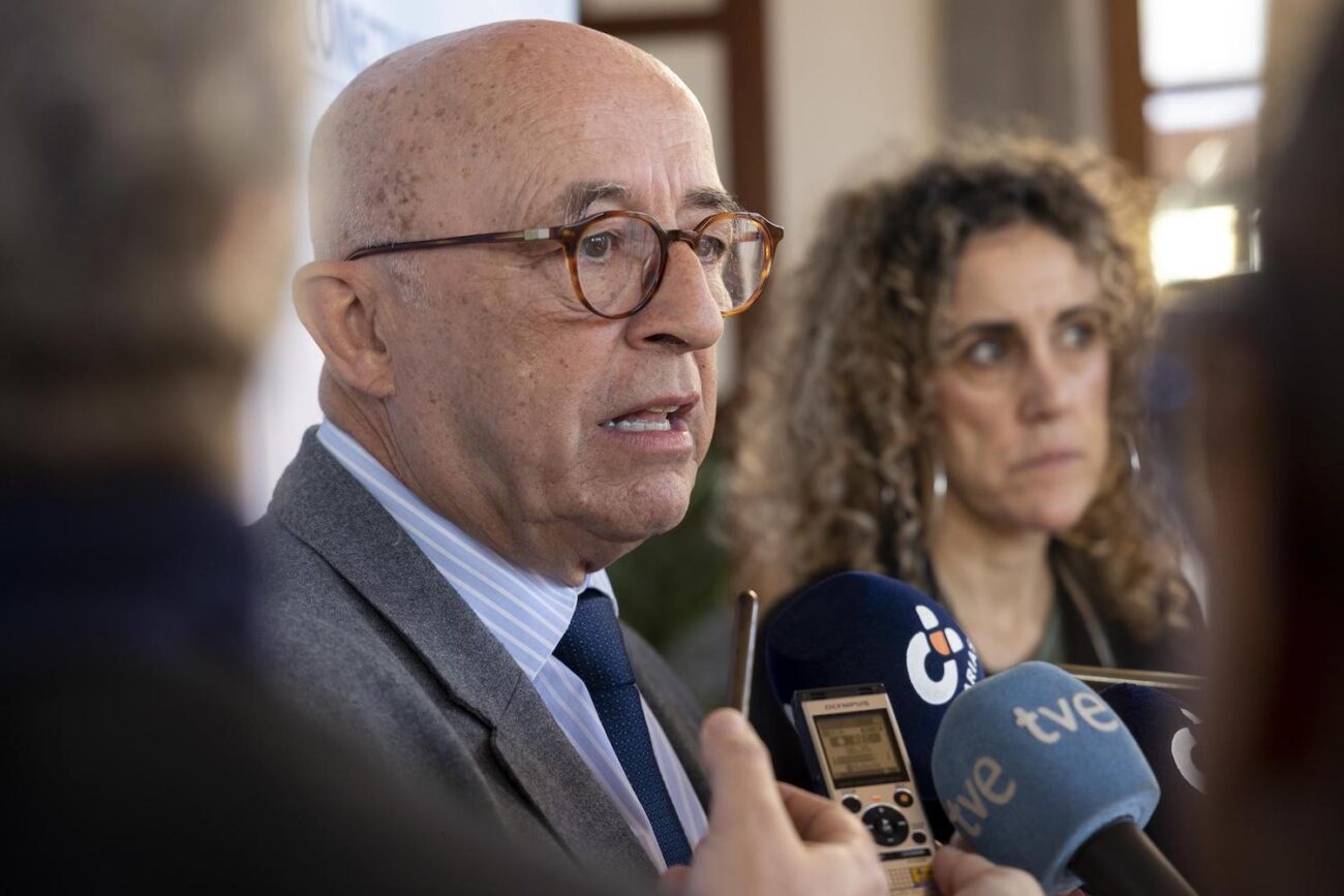 hombre calvo con gafas hablando a varios micrófonos